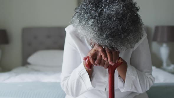 Senior african american woman holding walking stick sitting on the bed at home