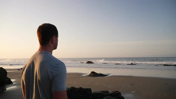 A strong good looking man watching the ocean waves and preparing for a morning workout on the beach