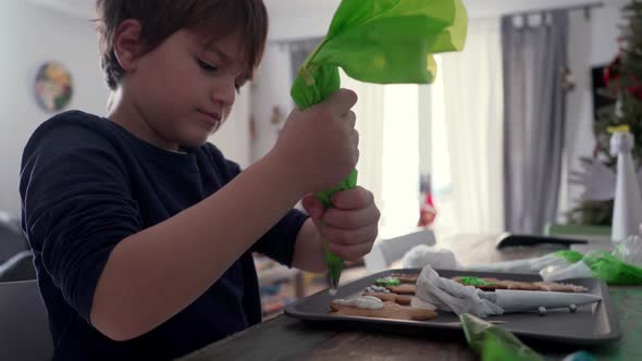 Caucasian kid decorates Christmas gingerbread cookies at home, using a pastry piping bag