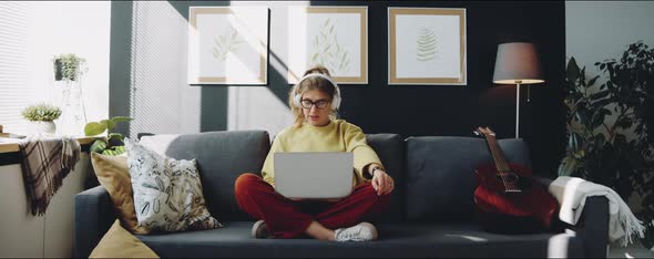 Woman in Headphones Singing and Using Laptop on Sofa at Home