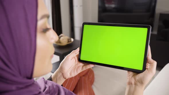 A Muslim Woman Looks at a Tablet (Horizontal) with Green Screen in an Apartment