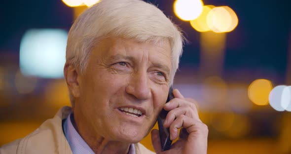 Bokeh Shot of Modern Senior Man Speaking By Smartphone Outdoors and Smiling