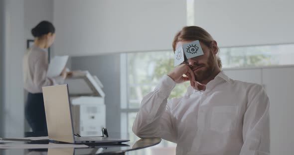 Young Tired Office Worker in Shirt Sitting at Desk at Workplace with Stickers on Eyes Napping