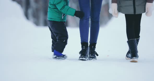 Mom with a Baby By the Hand and Daughter Goes on the Road in Winter