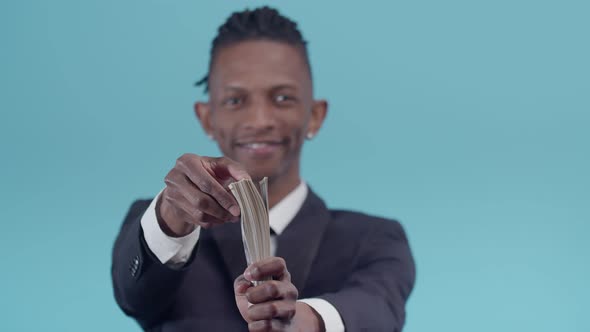 Black Male Businessman Smiling Holds a Pack of Dollar Bills in Hand and Flips Through Them with