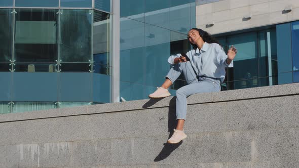 Happy Carefree Young Brunette Girl Woman Lady Sitting on Street in the City Urban Buildings