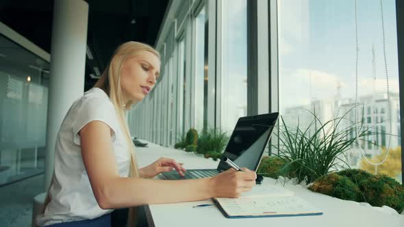 Formal Woman with Laptop and Papers. Side View of Businesswoman Writing on Paper While Sitting with