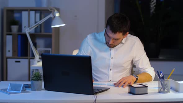 Businessman with Laptop and Papers at Night Office 1