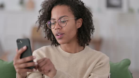 Portrait of Young African Woman Celebrating on Smartphone at Home 