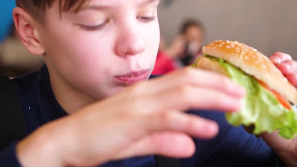 A Child Eats a Bun with a Cutlet and Cheese in a Fast Food Restaurant