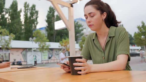 Caucasian woman drinking coffee in a cafe on the terrace and texting on the phone