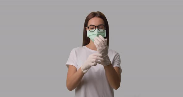 Woman in Medical Mask Putting on Her Medical Gloves, She Wears White T-shirt and Glasses, Isolated