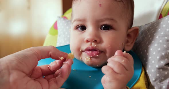 Mother Holds the Baby in Her Arms and Feeds Her Boy with a Spoon