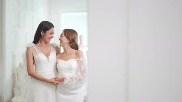4K Asian woman lesbian couple trying on wedding dress in front of the mirror together at bridal shop