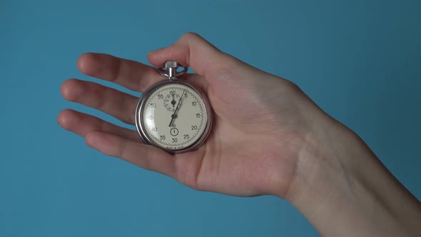 A woman's hand holds an analog stopwatch on a blue chromakey screen
