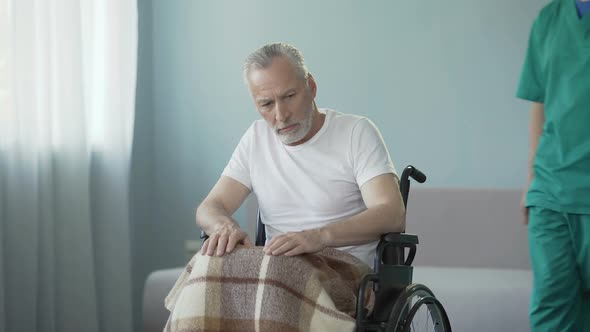 Paralyzed senior man in wheelchair shows no reaction to nursing house employee
