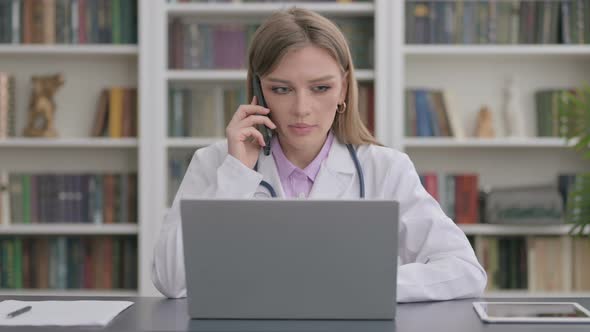 Lady Doctor Talking on Smartphone While Using Laptop in Clinic