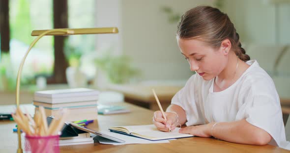 Closed Focused Teen Girl at the Desk Writes in Notebook and Scrolls Tablet Pencils Lamp Tablet