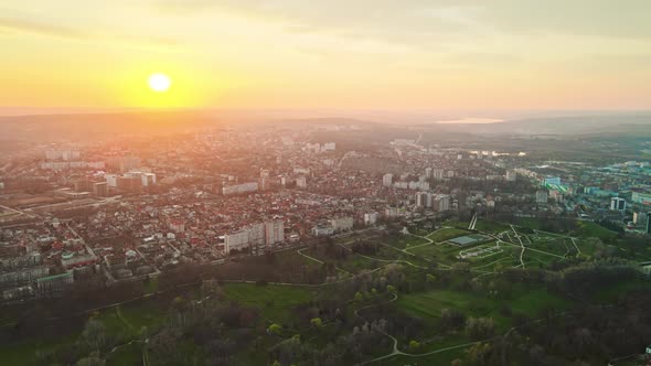 Aerial drone view of Chisinau at sunset. Multiple buildings, trees, park, setting sun. Moldova