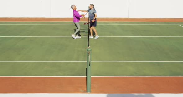 Video of happy biracial senior couple embracing after match on tennis court