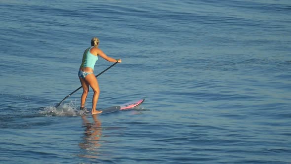 A young woman SUP surfing in a bikini on a stand-up paddleboard surfboard.