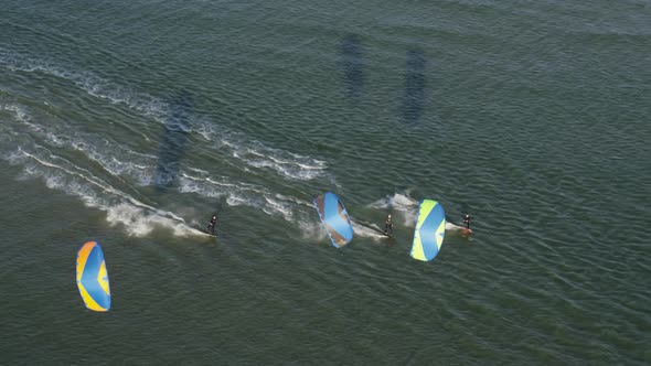 Three kite surfers glide across the ocean water while the one in the middle does acrobatic tricks in