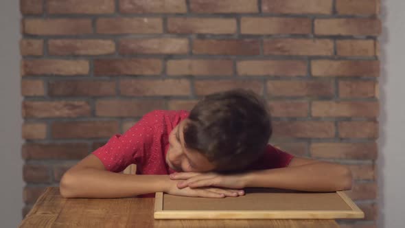 Child Sitting at the Desk Holding Flipchart with Lettering Wake Up on the Background Red Brick Wall.