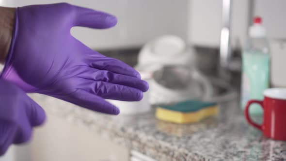 Young man in clothes pulls on his left blue protective glove for washing dishes