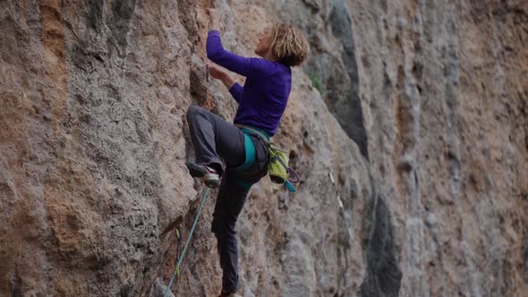 Athletic Adult Woman Rock Climber Climbs Up on Mountain Rock Wall Searching and Reaches Holds