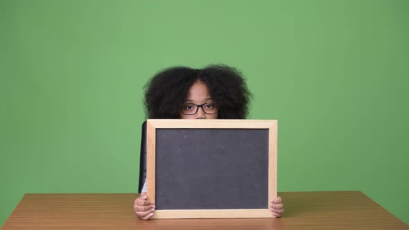 Young Cute African Girl with Afro Hair Showing Blackboard While Sitting