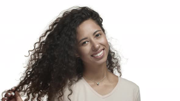 Closeup of Flirty Young Woman with Long Curly Hairstyle Smiling Coquettish and Playing with Hair to