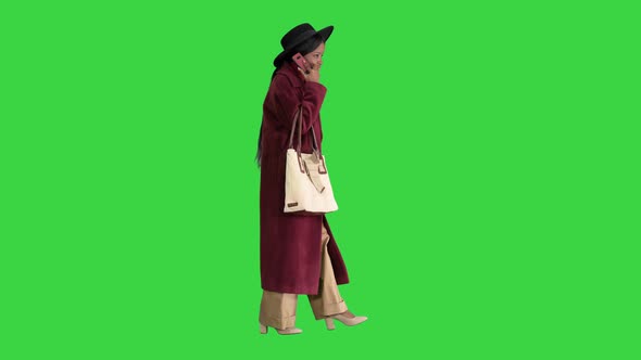 African American Fashion Girl in Coat and Black Hat Talking on the Phone While Walking on a Green
