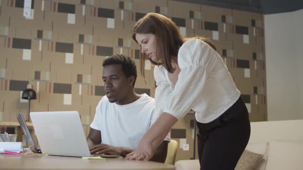 Diverse Coworkers Sitting and Standing at Table with Laptop