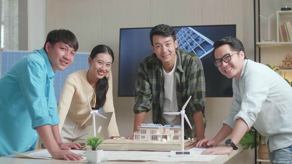 Asian Engineers Group Smiling To Camera While Working About Small House Model With Solar Panel