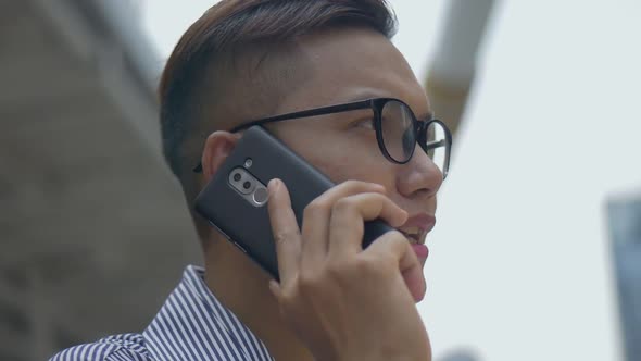 Asian men with glasses use phones in street near big office buildings.