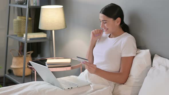 Latin Woman Online Shopping Success on Laptop in Bed 