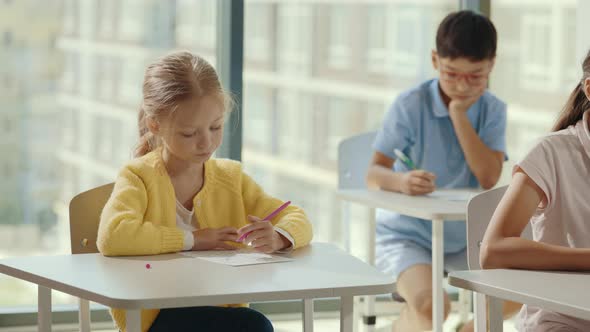 Female Caucasian Pupil Doing Test Carefully and Listening the Teacher and Other Pupils Filling Tests