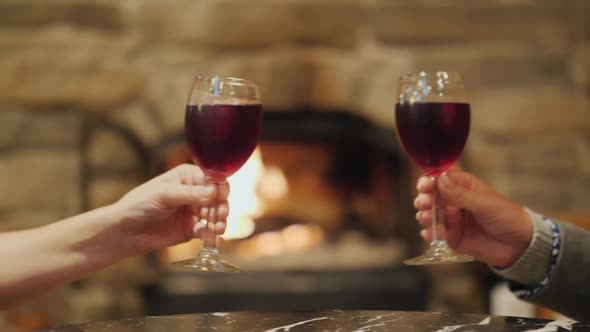 Two Hands with Glasses of Wine, Clinking in the Background of a Burning Fireplace