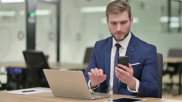 Businessman with Laptop Using Smartphone at Work