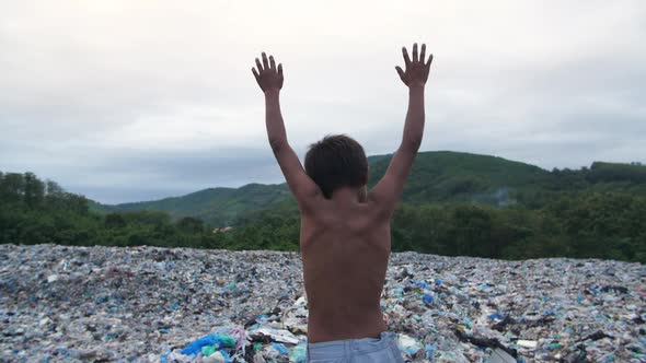 Poverty Boy Standing On Garbage Dump With Arms Raised