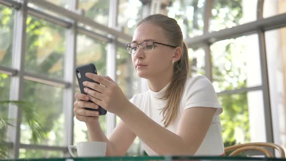 Woman Texts with Mobile Phone Sitting at Table with Coffee