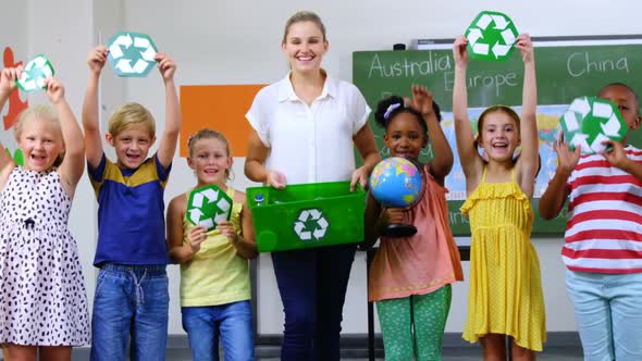 School kids and teacher holding recycling symbols and globe in classroom