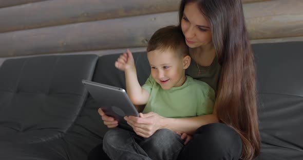 Young Smiling Mother and Her Sweet Son Playing in a Child Development App on a Digital Pill in a