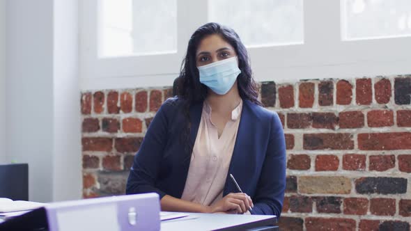 Portrait of woman wearing face mask sitting on her desk at office
