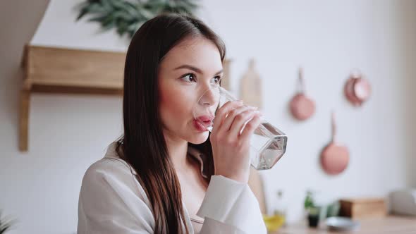 Young Brunette Woman Enjoys Drinking Water in Glass at Home