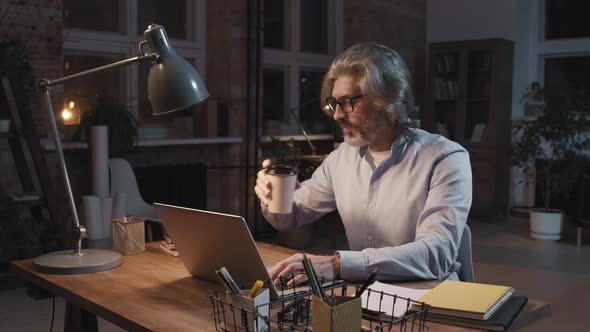 Mature Office Worker Typing On Laptop At Night