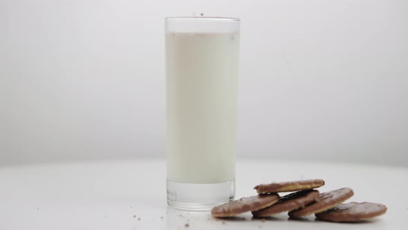 Sweet Biscuits and Glass of Milk on Table Closeup with Chocolate Powder Falling on Food and Drink