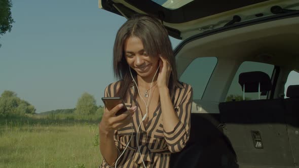 Carefree Lovely Black Woman Traveler in Car Trunk Enjoying Music in Nature