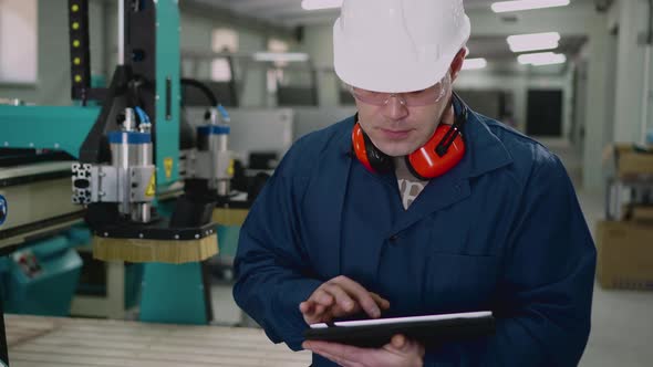 A Male Factory Worker Uses a Tablet in the Workshop