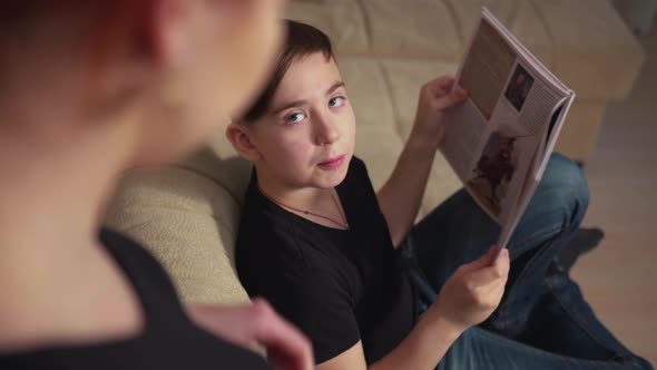 Mother with Red Hair Talks to Young Son Reading Book on Sofa